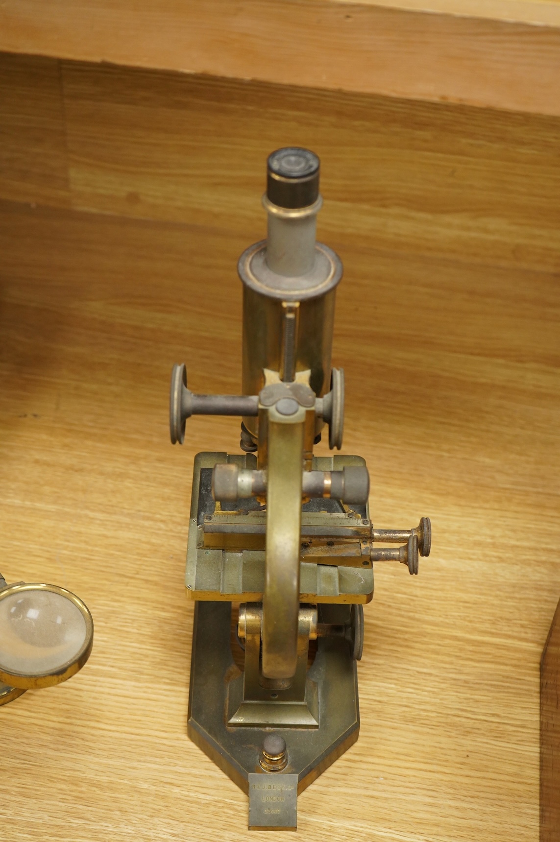 An early 20th century brass compound monocular microscope, by R & J Beck, Ltd., London, number 33007, with accessories including spare lenses, a free standing magnifier and objectives, mahogany cased; 34.5cm high, 19cm w